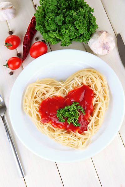 اسپاگتی پخته شده با دقت به شکل قلب چیده شده و با سس گوجه فرنگی روی زمینه چوبی ریخته شده است