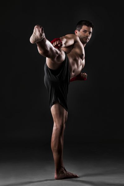 پرتره مردی عضلانی که در حال تمرین مبارزه با بدن در پس زمینه ای تاریک است