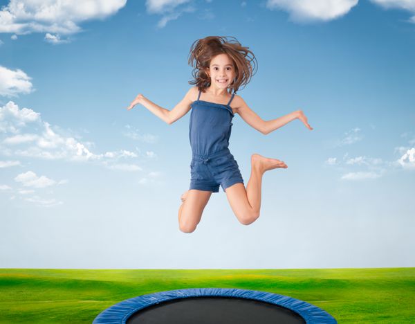 دختری شاد در حال پریدن روی یک چمنزار روی ترامپولین