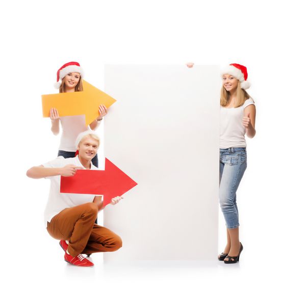 سه نوجوان شاد با کلاه کریسمس که روی یک بنر بزرگ خالی با یک فلش قرمز اشاره می کنند