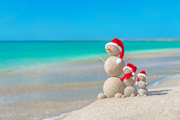 خانواده آدم برفی در ساحل دریا با کلاه بابا نوئل مفهوم سال نو و تعطیلات کریسمس در کشورهای گرم