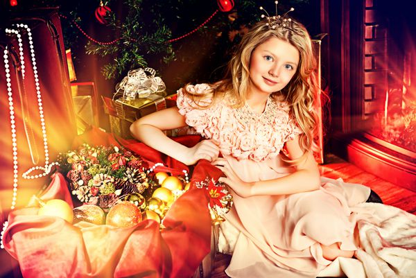 دختر ده ساله ناز در خانه روی زمینی نزدیک درخت کریسمس و شومینه نشسته است