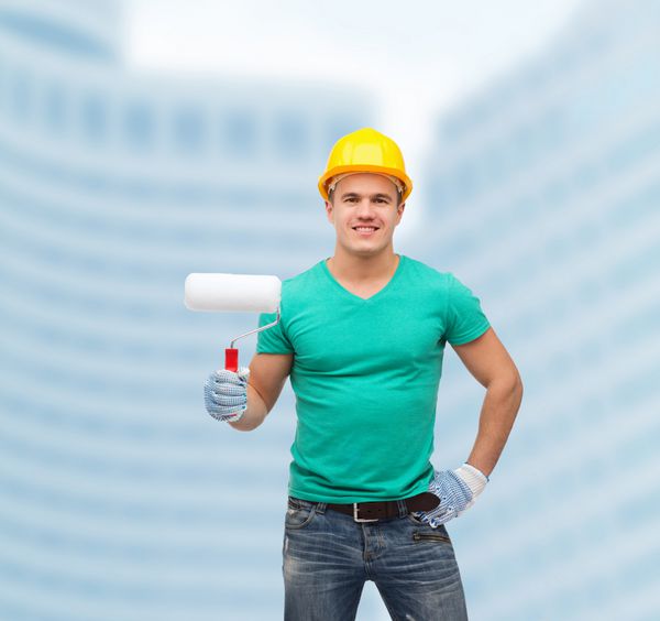 مفهوم تعمیر ساخت و نگهداری - کارگر دستی مرد خندان در کلاه ایمنی با غلتک رنگ