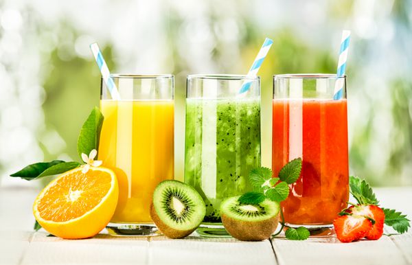 مجموعه ای خوشمزه از آب میوه های تازه در لیوان های بلند ساخته شده از پرتقال مایع کیوی با نعناع و توت فرنگی برای غذاهای تابستانی سالم و سرشار از ویتامین سرو می شود