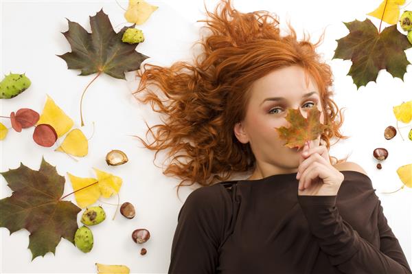 پرتره یک زن جوان مو قرمز که بینی خود را پشت یک برگ پاییزی پنهان کرده است