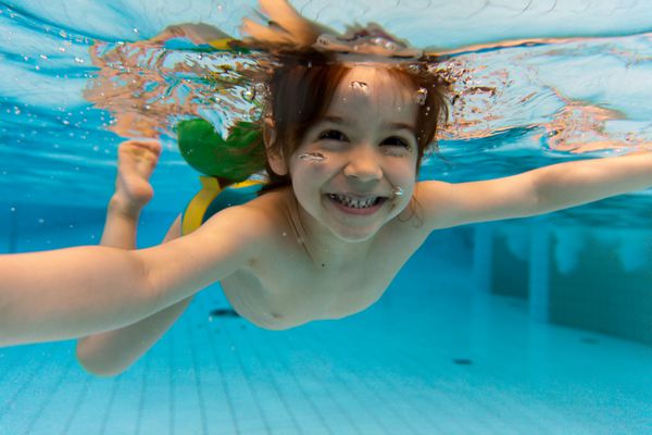 دختر کوچکی که در پارک آبی زیر آب شنا می کند و لبخند می زند