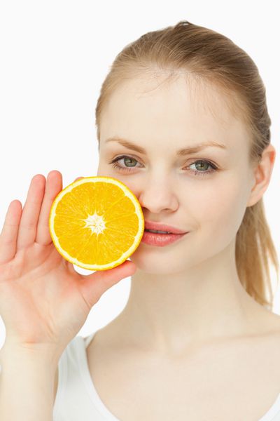 زنی که یک پرتقال روی لب هایش در برابر پس زمینه سفید می گذارد