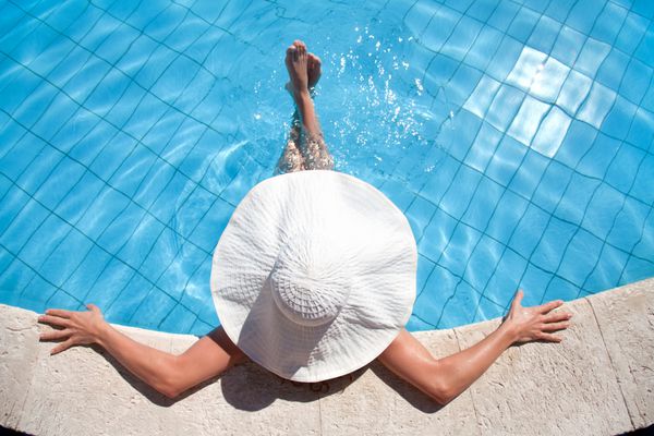 زن ناشناخته با کلاه بزرگ در حال استراحت در استخر شنا