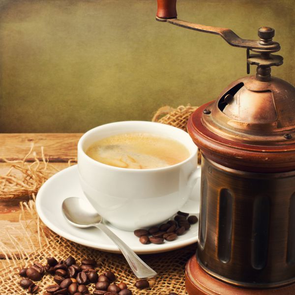 آسیاب قهوه قدیمی و فنجان قهوه روی پس زمینه چوبی
