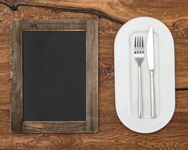 تخته سیاه برای منو روی میز چوبی با بشقاب سفید چاقو و چنگال