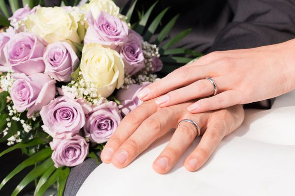 دست های نزدیک زن و شوهری که حلقه ازدواج پوشیده و دسته گل در دست دارند