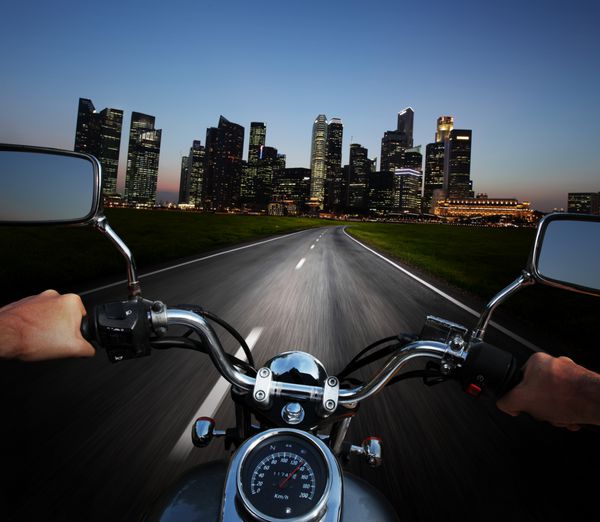 راننده موتور سواری در جاده آسفالته در شب به سمت شهر بزرگ