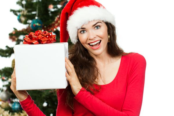 یک زن غافلگیر شده خوشحال که کلاه بابانوئل بر سر دارد و یک هدیه کریسمس سفید بزرگ با فضایی برای کپی در دست دارد جدا شده روی سفید
