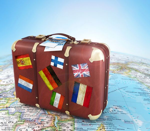 چمدان قدیمی با بلیط هواپیما و پرچم های راه راه روی نقشه جهان تار و آسمان در پس زمینه