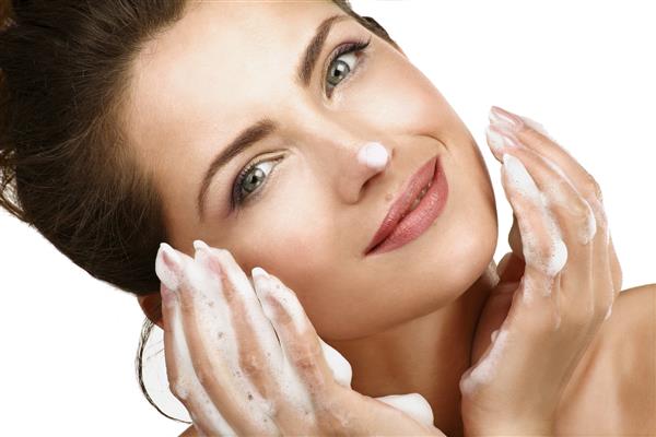 زن زیبا در حال تمیز کردن صورت خود با فوم درمانی روی سفید