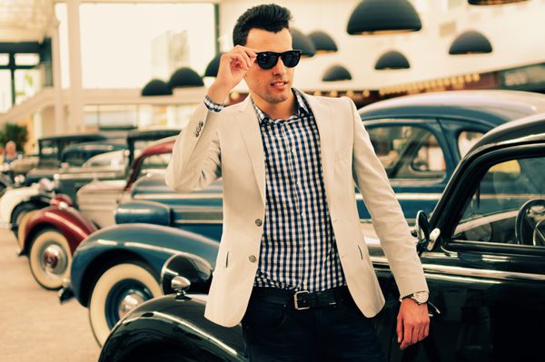 پرتره یک مرد جوان خوش تیپ مدل مد پوشیدن ژاکت و پیراهن با ماشین های قدیمی