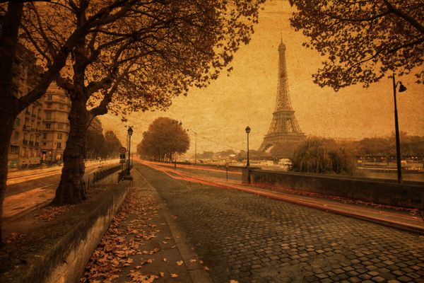 تصویری قدیمی از پاریس در غروب با خیابانی در امتداد رود سن و برج ایفل در پس‌زمینه