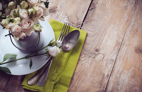 چیدمان میز قدیمی با گل های رز روی دستمال سفره کتان روی پس زمینه تخته چوبی نمای نزدیک
