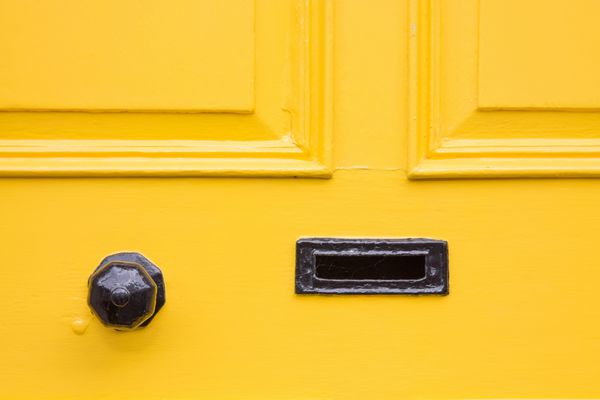 جزئیات یک درب ورودی زرد با دستگیره سیاه و جعبه نامه