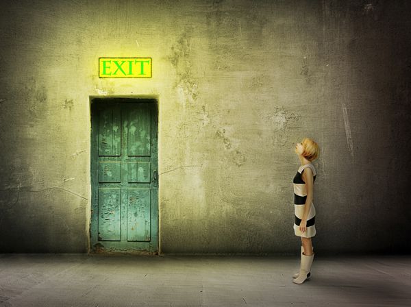 زن جوان با لباس سیاه و سفید جلوی در آبی با ساعت اتاق تیره رنگی روی تابلوی خروجی درخشان ایستاده - راه خروج را پیدا کنید