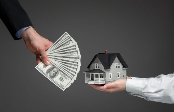 نمای نزدیک از دست هایی که مدل خانه را با پول به دست های دیگر می دهد مفهوم املاک و مستغلات و معامله
