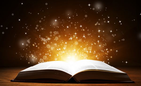 کتاب باز قدیمی با نور جادویی و ستاره های در حال سقوط روی میز چوبی