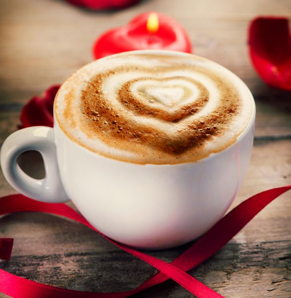 قهوه روز ولنتاین با قلب روی فوم طراحی قلب روی قهوه کاپوچینو یا لاته آرت عشق طراحی هنری ولنتاین فنجان قهوه روی میز چوبی شمع قلبی شکل گلبرگ های رز و روبان ساتن