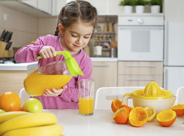 کودک در حال ریختن آب پرتقال تازه آماده برای نوشیدن