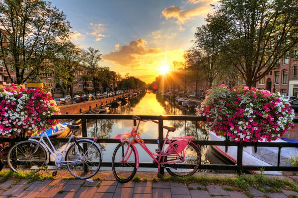 طلوع زیبای آفتاب بر فراز آمستردام هلند با گل و دوچرخه روی پل در بهار