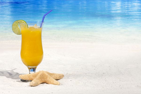 کوکتل گرمسیری با پرتقال و نی نوشیدنی در ساحل با ستاره دریایی و فضای کپی زیاد