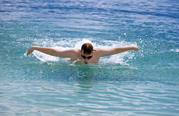 مرد جوان ورزشکار به سبک شنای پروانه دریایی شنا می کند