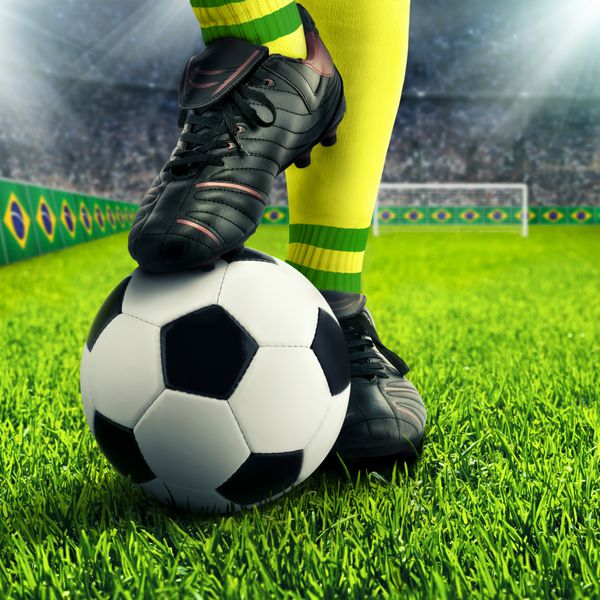 پاهای فوتبالیست برزیلی در ژست معمولی در یک میدان فوتبال با جمعیت در پس زمینه