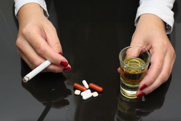 زن ویسکی و سیگار را در دست دارد و مواد مخدر را روی میز نگه می دارد