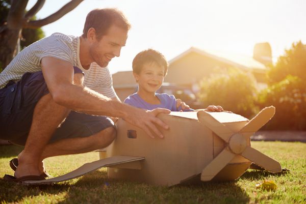 پسر و پدر در حال بازی با هواپیمای اسباب‌بازی در باغ در خانه و با هم سرگرم می‌شوند و لبخند می‌زنند