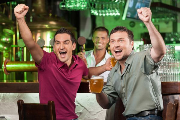طرفداران فوتبال در بار دو هوادار شاد فوتبال در حال تشویق در بار و نوشیدن آبجو در حالی که متصدی بار در حال سرو آبجو در پس زمینه است