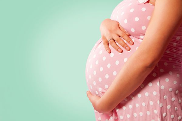 نمای نزدیک از زن باردار ناشناخته با دست روی شکم بر روی پس زمینه سبز