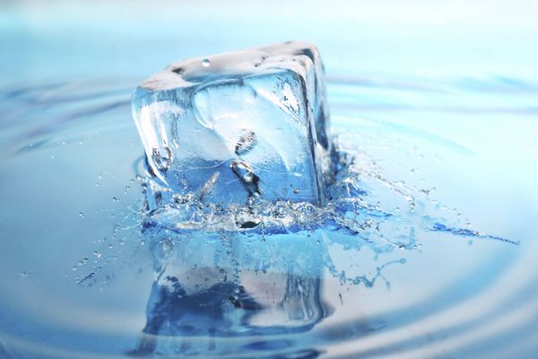 یک مکعب یخ با طراوت در آب تازه ریخته شده است پاشش های یخ زده در زمان