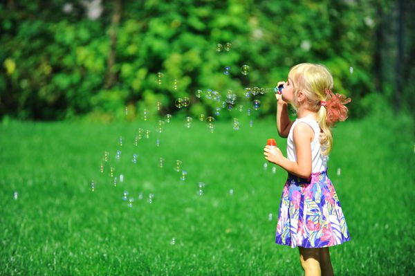 بازی دختر بچه با دمنده حباب در چمن سبز