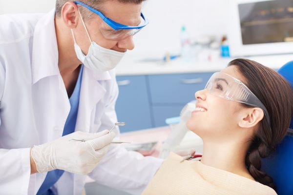 دختر جوان شادی که در حین معاینه دهان به دندانپزشک نگاه می کند