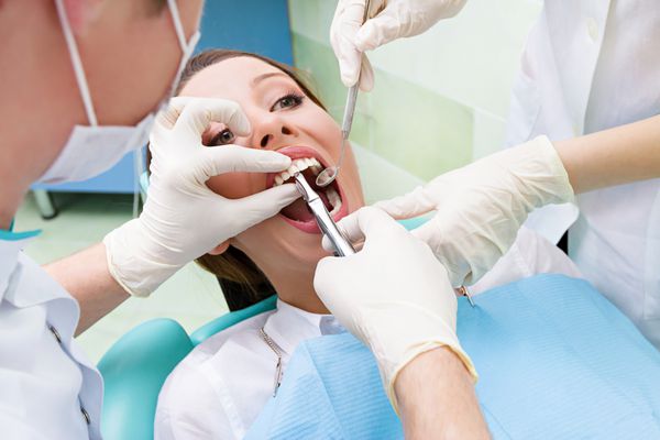 دندانپزشک پرتره نزدیک دستیار او در حال انجام معاینه کامل دندانپزشکی کشیدن دندان در بیمار زن جوان دراز کشیده روی صندلی پس زمینه مطب کلینیک ایزوله با دهان باز