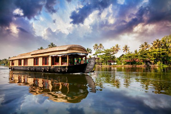 قایق خانگی در آبهای پس‌آب نزدیک نخل‌ها در آسمان آبی ابری در آلاپوزا کرالا هند