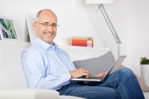 مرد خندان روی مبل نشسته و در حال گشت و گذار در اینترنت است
