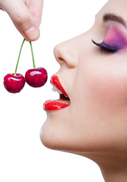 از نزدیک دختری با لب‌های قرمز و آرایش روشن در حال خوردن دو توت جدا شده روی سفید مفهوم و سلامتی