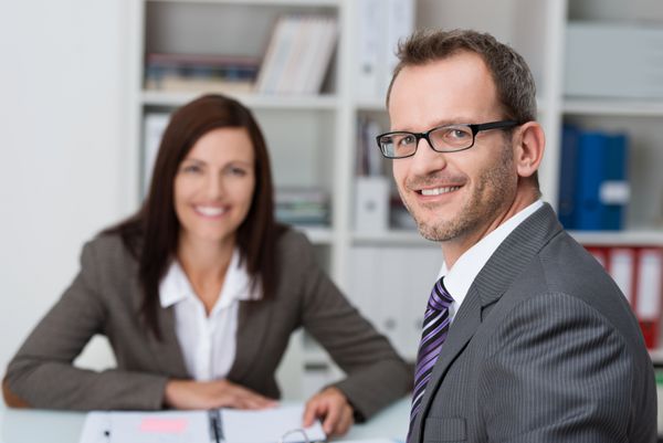تاجر خوش تیپ خندان با عینک در دفتر با یک همکار زن نشسته است