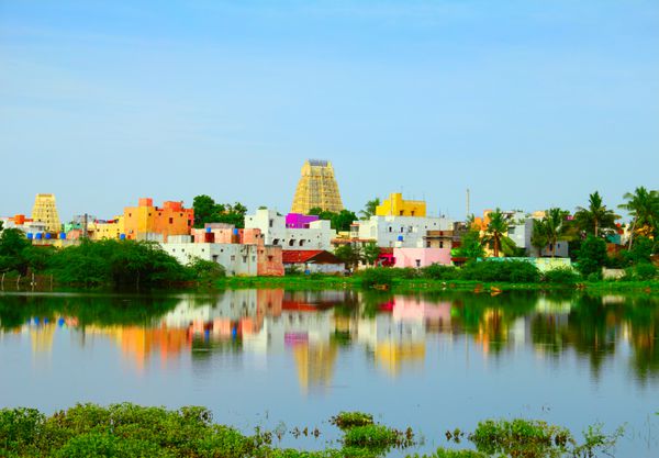 منظره زیبای شهر مقدس کانچیپورام کانچی با خانه‌های سنتی رنگارنگ گوپورای معبد هندو و شاخ و برگ‌های درخشان که در آب‌های آرام دریاچه تامیل نادو جنوب هند منعکس شده است