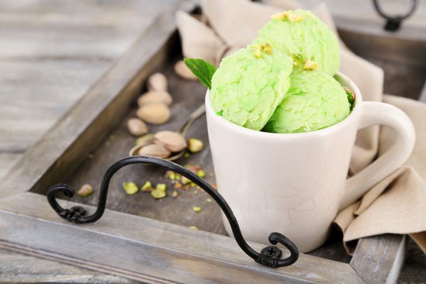 بستنی پسته خوشمزه در فنجان روی میز چوبی