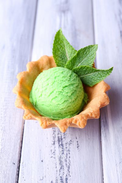 توپ بستنی سبز در کاسه ویفر در زمینه چوبی رنگی