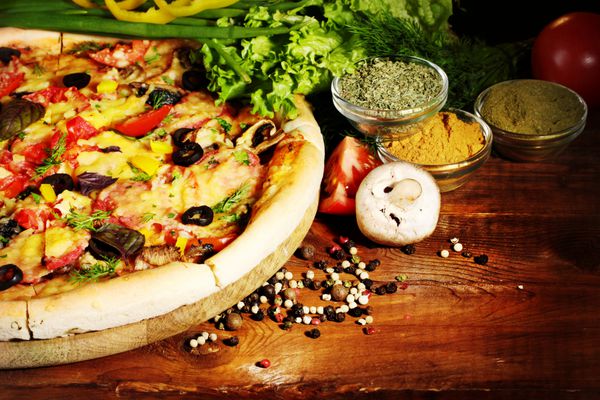 پیتزا سبزیجات و ادویه های خوشمزه روی میز چوبی