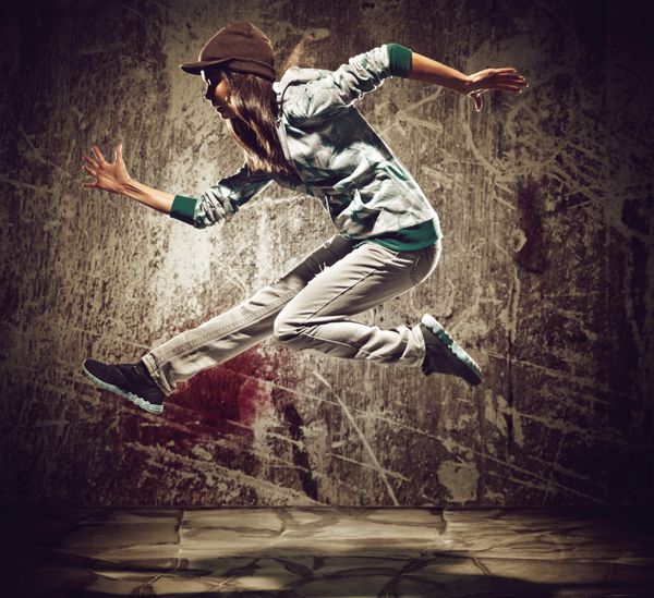 رقصنده هیپ هاپ شهری با بافت پس زمینه دیوار بتنی گرانج که با هودی می پرد و می رقصد