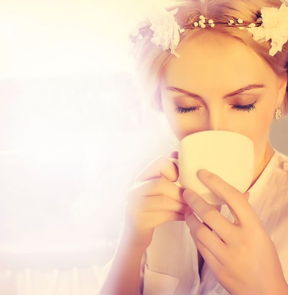 زن زیبا در حال نوشیدن قهوه زنی با فنجان قهوه پشت پنجره